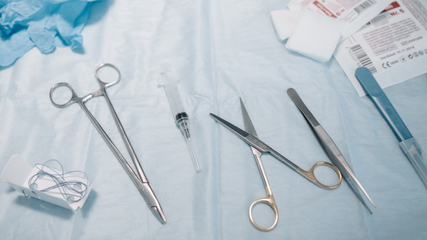 Medical scissors, gloves, needles, and sharps on a blue table cloth